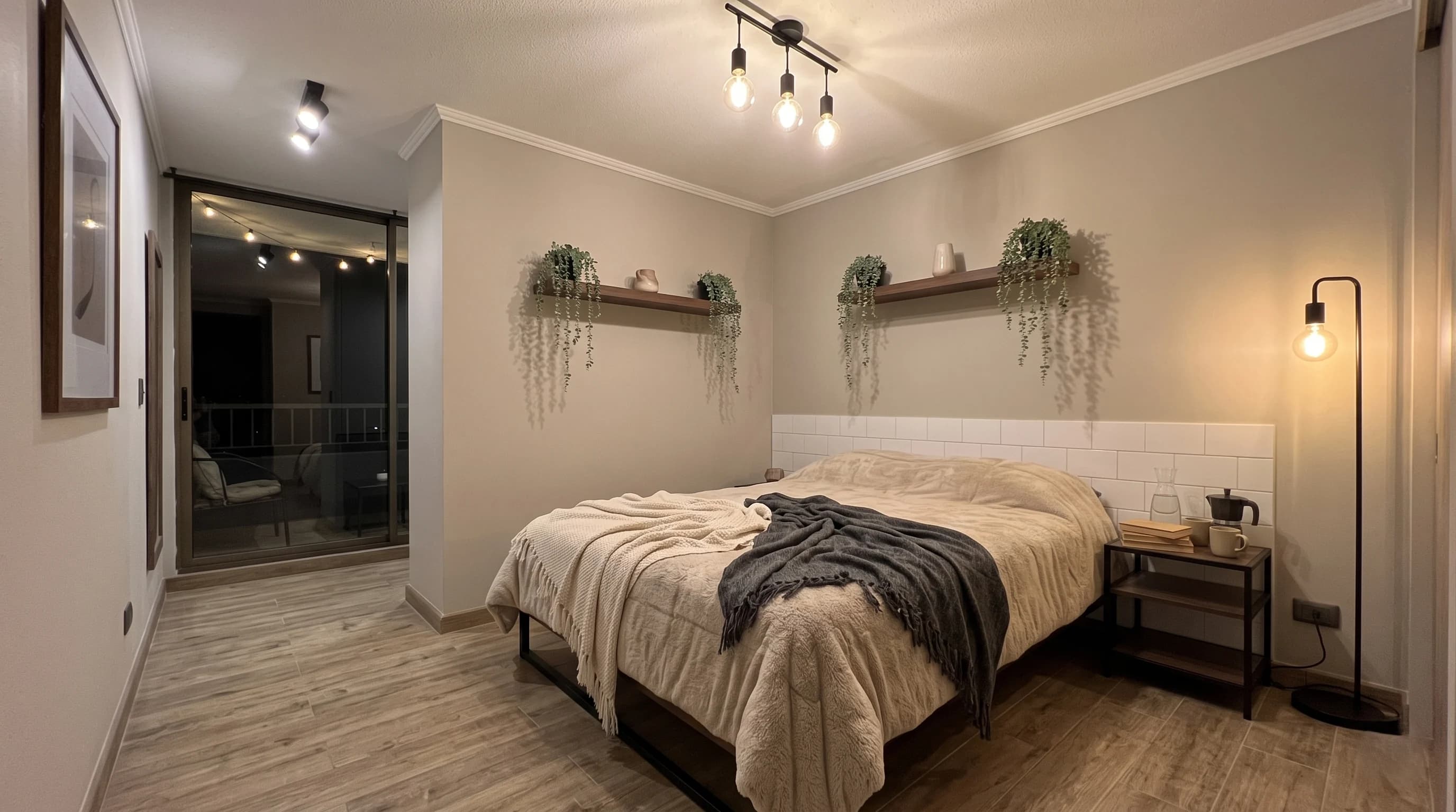 Habitación cálida con ropa de cama en tonos tierra, plantas colgantes sobre repisas de madera y lámpara de luz tenue.